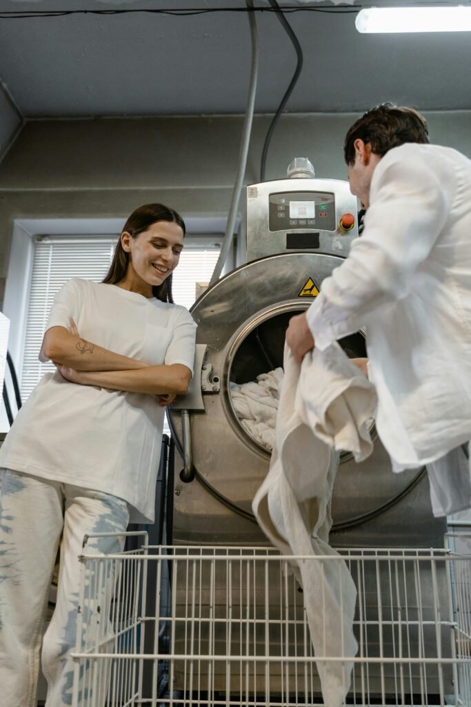 Two young adults doing laundry in a modern facility, using industrial washing machines.